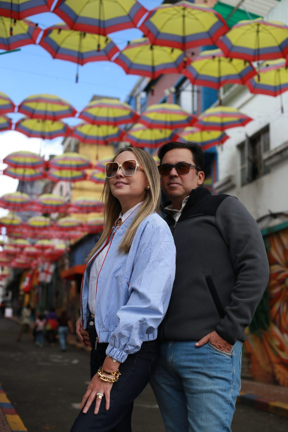 Casal posando sob guarda-chuvas coloridos em uma rua